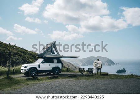 Couple sitting in a camping chair in nature with a view of Island in a beautiful blue sky with an overlanding car with a rooftop tent and an awning. Royalty-Free Stock Photo #2298440125