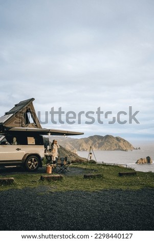 Couple sitting in a camping chair in nature with a view of Island in a beautiful blue sky with an overlanding car with a rooftop tent and an awning. Royalty-Free Stock Photo #2298440127