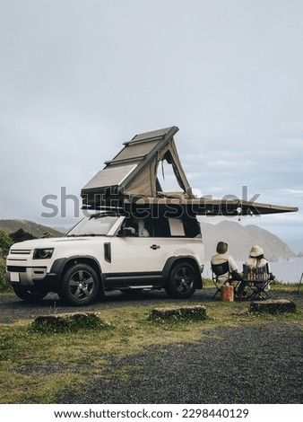 Couple sitting in a camping chair in nature with a view of Island in a beautiful blue sky with an overlanding car with a rooftop tent and an awning. Royalty-Free Stock Photo #2298440129