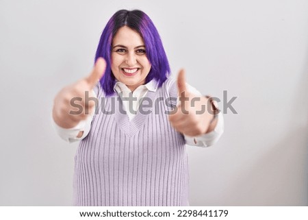 Plus size woman wit purple hair standing over white background approving doing positive gesture with hand, thumbs up smiling and happy for success. winner gesture. 