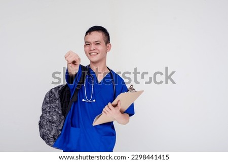 Portrait of a young and bubbly medical student, intern, nurse on the way to work wearing a backpack and holding a checklist board while pointing at the camera. Isolated on a white background.