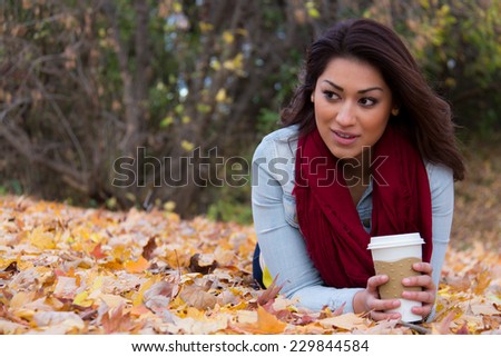 Girl lying on autumn leaves with coffee looking away