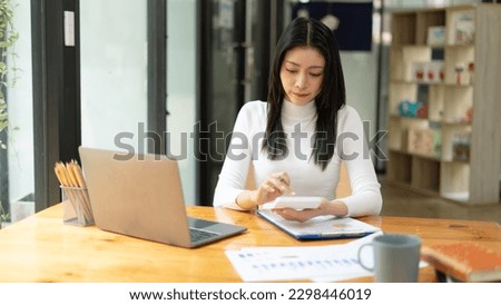 Businesswoman using calculator and laptop for doing math finance on an office desk.