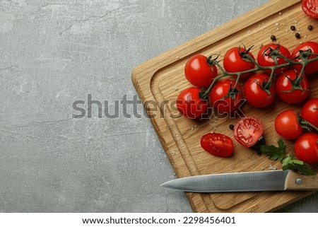 Cutting board with cherry tomato and knife on gray textured background