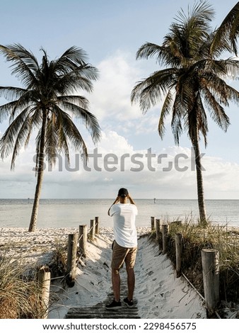 Man taking pictures at Smathers Beach, Key West, Florida, USA on a beautiful day against blue sky with clouds