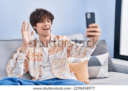Young hispanic man having video call sitting on sofa at home