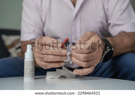 Grandfather cleaning his hearing aids so he can listen. Royalty-Free Stock Photo #2298464521