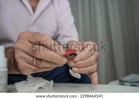 Grandfather cleaning his hearing aids so he can listen. Royalty-Free Stock Photo #2298464541