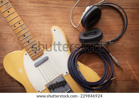 Guitar recording. An electric guitar, and a professional use headphones on a rustic or bare wooden table, with by-the-window type warm light coming in. 