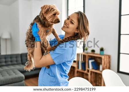 Young beautiful hispanic woman veterinarian smiling confident holding dog at home Royalty-Free Stock Photo #2298475199