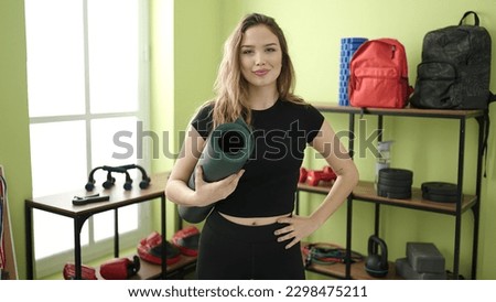 Young beautiful hispanic woman smiling confident holding yoga mat at sport center