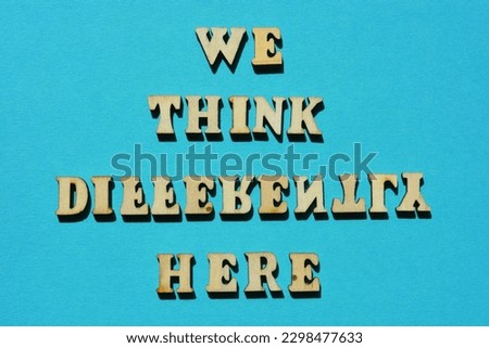 We Think Differently Here, words in wooden alphabet letters isolated on blue background