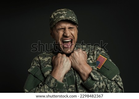 stressed soldier in uniform with USA flag screaming while suffering from panic attacks isolated on black