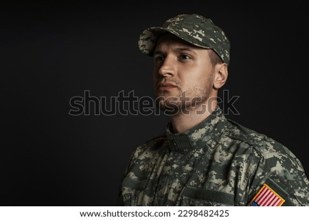 patriotic soldier in uniform with American flag looking away isolated on black