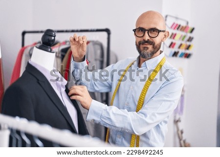 Young bald man tailor smiling confident working at tailor shop Royalty-Free Stock Photo #2298492245
