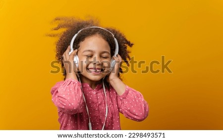 An African-American little girl with headphones listens to music expressing real emotions. Royalty-Free Stock Photo #2298493571