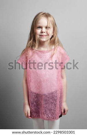A cute and happy girl with long blonde hair wearing a pink knitted sweater on a grey background
