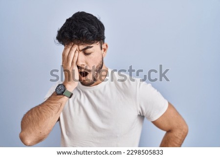 Hispanic man with beard standing over white background yawning tired covering half face, eye and mouth with hand. face hurts in pain.  Royalty-Free Stock Photo #2298505833