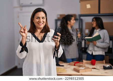 Three women working at small business ecommerce smiling happy pointing with hand and finger to the side  Royalty-Free Stock Photo #2298512505