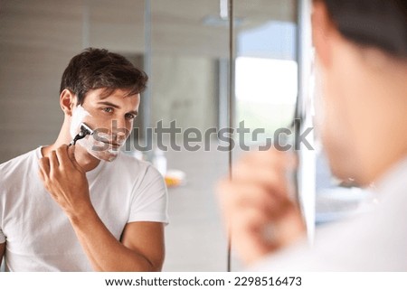 Mirror, shaving and face of man in bathroom for facial grooming, wellness and skincare at home. Health, skincare and serious male person shave beard for hygiene, cleaning and hair removal with razor Royalty-Free Stock Photo #2298516473