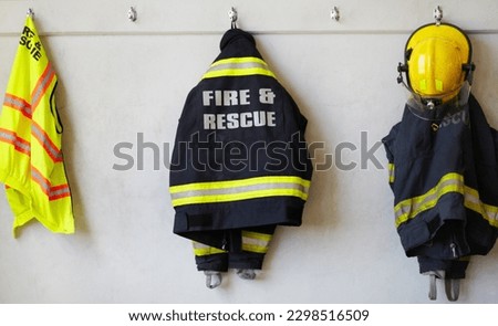Fireman, uniform and clothing hanging on wall rack at station for fire fighting protection. Firefighter gear, rescue jacket and helmet with reflector for emergency services, equipment or department Royalty-Free Stock Photo #2298516509