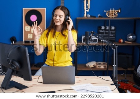 Young hispanic girl listening to music wearing headphones doing ok sign with fingers, smiling friendly gesturing excellent symbol 