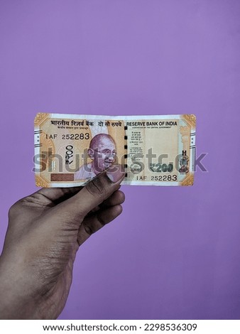 Indian currency, 200 rupees note held by a brown man on a purple background. Gandhi photo on Indian rupee