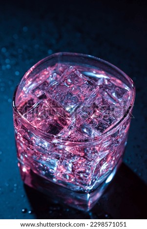 Glass of cold water with ice with colored lighting on a black background. refreshing drink