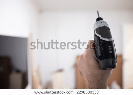 Man with a drill is preparing to assemble furniture at home with his own hands, no face, real photo. DIY hand craft carpenter. Electric screwdriver, tool, do-it-yourself tool, handyman, carpenter