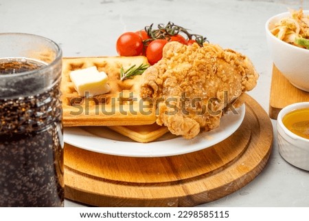 Deep-fried chicken and waffles on a wooden board served with butter and a drink. Vertical photo.