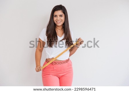 Beautiful Brazilian woman, nutritionist, weight loss, white shirt and pink pants. advertising photo, measuring tape for body measurement.