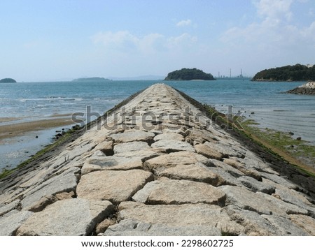 A stone breakwater extending into the sea.
A landscape of a Japanese fishing port located on the coast of an inland sea in Japan.
A stone structure to keep waves from entering into the port.
