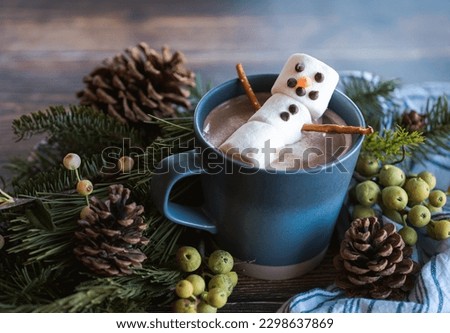 Marshmallow snowman in a mug of hot chocolate with winter decor.