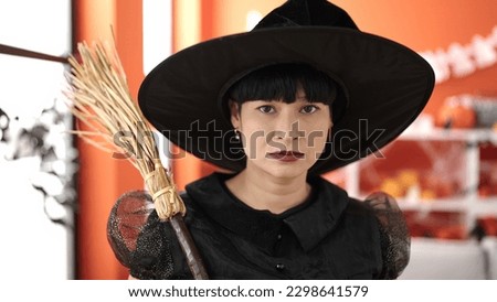 Young chinese woman wearing witch costume holding broom at home