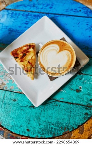 Large cup of cappuccino coffee and apple pie on colorful green and blue cafe table
