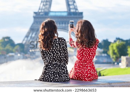 Beautiful twin sisters photographing the Eiffel Tower while traveling in Paris, France
