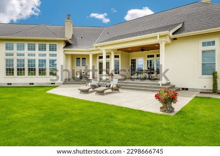 Large estate home on lush green grass landscaping blue sky elegant house has yellow paint three car garage rounded shape heavy wooden front door arched doorway and brick trim