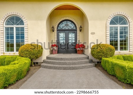 Large estate home on lush green grass landscaping blue sky elegant house has yellow paint three car garage rounded shape heavy wooden front door arched doorway and brick trim Royalty-Free Stock Photo #2298666755