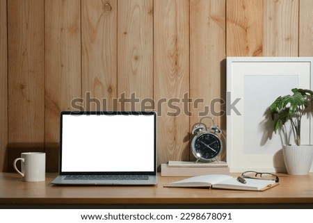 Front view of laptop computer, coffee cup, houseplant and picture frame on wooden table.