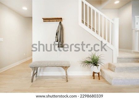 Bright and airy entry foyer with white wall stair case light colored hard wood flooring dark walnut front door entry coat rack hooks to a welcoming interior Royalty-Free Stock Photo #2298680339