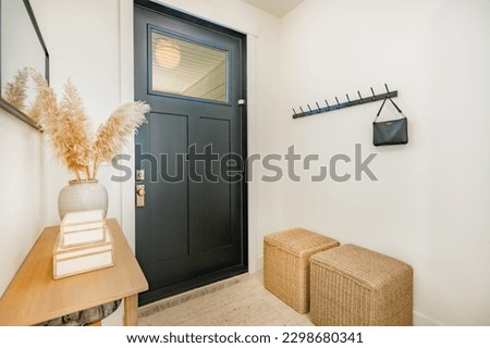 Bright and airy entry foyer with white wall stair case light colored hard wood flooring dark walnut front door entry coat rack hooks to a welcoming interior Royalty-Free Stock Photo #2298680341
