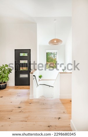 Bright and airy entry foyer with white wall stair case light colored hard wood flooring dark walnut front door entry coat rack hooks to a welcoming interior Royalty-Free Stock Photo #2298680345