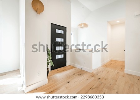 Bright and airy entry foyer with white wall stair case light colored hard wood flooring dark walnut front door entry coat rack hooks to a welcoming interior Royalty-Free Stock Photo #2298680353