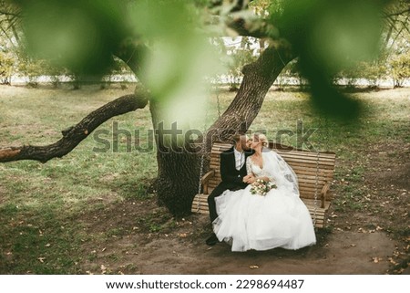 Wedding day. Happy beautiful family couple. Groom hugs bride on the swing after wedding ceremony. Royalty-Free Stock Photo #2298694487