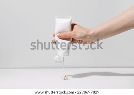 A female hand squeezes a body cream or scrub from a blank tube on a white plain background. Cosmetic product and self care concept. Place for your design Royalty-Free Stock Photo #2298697829