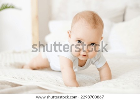 close-up of a happy baby on a white cotton bed in a bright bedroom, a small smiling baby boy or girl crawling Royalty-Free Stock Photo #2298700867