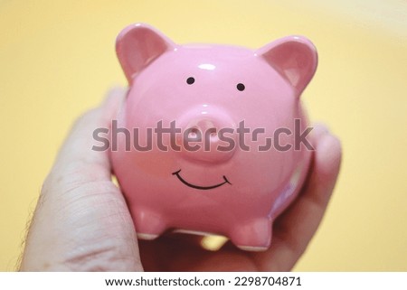 A man holding a piggy bank in his hand. Close-up photo. Orange background.
