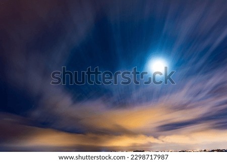 Moon in the blue night sky, with clouds streaking across the sky.