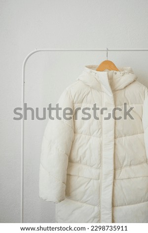 Outerwear hanging on a wooden hanger, a white hooded jacket hanging on a white background, free space, template.