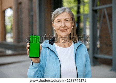 Mature Smiled Woman Holds Smartphone with Green Screen on the Street Background. Advertising Concept Promotional Offers. Technology Concept